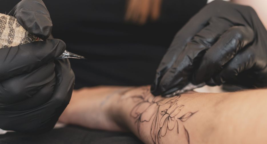a gorgeous tattoo of a flower on woman's hand, tattoo artist in the process of work